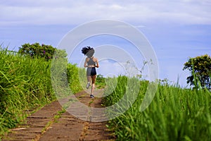 Rear view female runner training on countryside road - young attractive and fit jogger woman doing running workout outdoors at