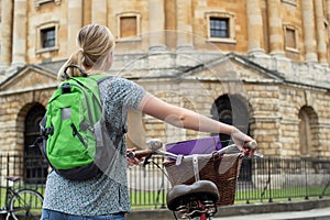Rear View Of Female Student Riding Old Fashioned Bicycle Around Oxford University College Buildings By Radcliffe Camera In