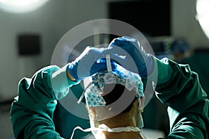 Rear view of female surgeon in surgical cap and gloves tying mask in operating theatre