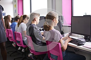 Rear View Of Female Teacher Supervising Line Of High School Students Working at Screens In Computer Class
