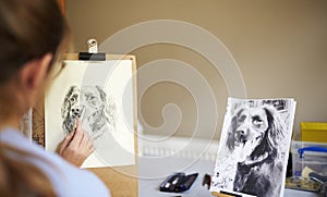 Rear View Of Female Teenage Artist Sitting At Easel Drawing Picture Of Dog From Photograph In Charcoal