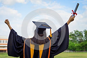 Rear view of a female university graduate stands and holds degree certificate to celebrate in the  graduation ceremony with clear