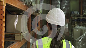 Rear view of a female worker in a protective vest and helmet as she walks through the warehouse