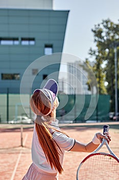 Rear view on forceful fit woman playing tennis in outdoor court, hitting ball, training