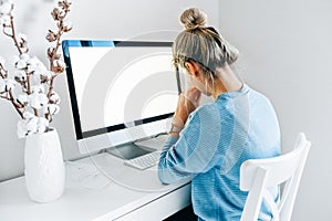 Rear view of a freelacer businesswoman using desktop computer in the office. Pretty young blonde woman sit indoors at home working