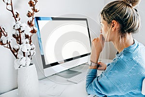 Rear view of a freelacer businesswoman using desktop computer in the office. Pretty young blonde woman sit indoors at home working