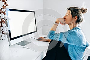 Rear view of a freelacer businesswoman using desktop computer in the office. Pretty young blonde woman sit indoors at home working