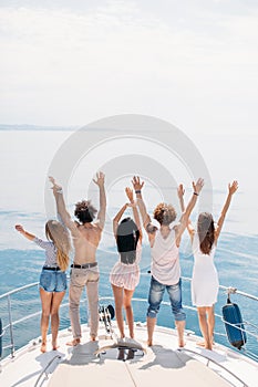 Rear view of friends celebrate on sailboat in ocean, arms raised.
