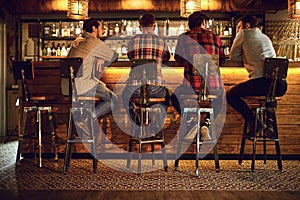 Rear view friends sitting on chairs talking at the bar in a bar.