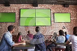 Rear View Of Friends Watching Game In Sports Bar On Screens