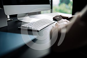 Rear view of a girl in a classic shirt who works at a computer in the office holding a mouse in her hands and a graphic tablet.