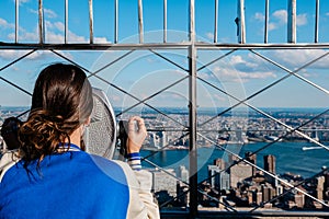 Rear view of girl looking at view of manhattan skyline with binoculars from the Empire State Building