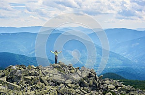 Rear view girl is opening her arms standing on top of cliff with powerful view mountain valley