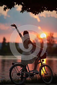 Rear view of girl with retro bike on which the basket enjoys the fiery sun at sunset