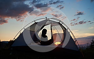Rear view girl sitting in tent under the morning blue sky enjoying the dawn