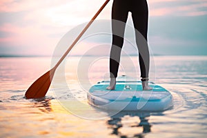 Rear view of girl surfer paddling on surfboard on the lake at sunrise, lowsection.