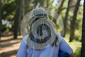 Rear view grizzle woman with dreadlocks walking on park in summer - stylish hairstyle and modern old men