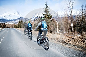 Rear view of group of mountain bikers riding on road outdoors in winter.