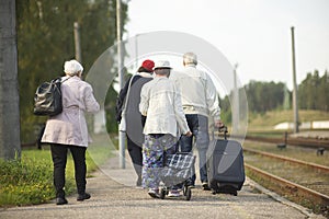 Rear view of a group of seniors elderly old people with luggage waiting for  train to travel