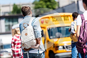 rear view of group of teen students with backpacks walking to school bus