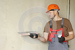 Rear view of handyman worker in overalls and protective helmet plastering concrete wall with putty using a big putty
