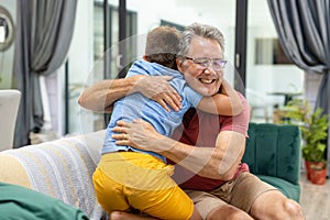Rear view of happy caucasian grandson embracing grandfather on sofa in living room, copy space