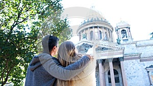 Rear view of a happy couple standing and discussing amazing temple near green bush. Concept. Man hugging woman, looking