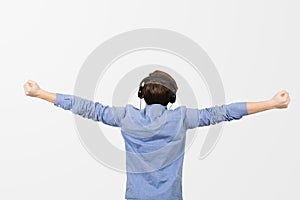 Rear view of happy student listening to music with arms raised in air over white background. Young boy student relaxing  listening