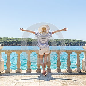 Rear view of happy woman on vacation, wearing straw summer hat ,standing on luxury elegant old stone balcony of coastal