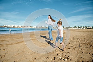Rear view of a happy young mother and daughter smiling while running on the beach, leaving footsteps on the wet sand