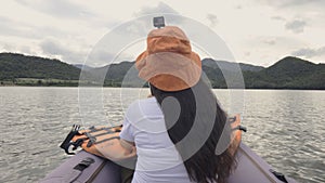 Rear view of happy young woman taking photo or selfie on kayak boat on water of large mountain lake. Summer travel, adventure, ho