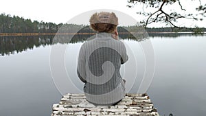 Rear view, a hiker sits on the shore of a lake and talks on the phone. Sadness and loneliness, longing concept