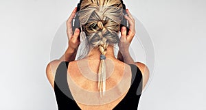 Rear view image of a blonde young woman touching her headphones during listening to music. Horizontal back view of pretty female