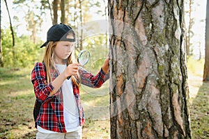 Rear view image of cute little girl exploring the nature with magnifying glass outdoor. Child playing in the forest with