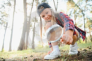 Rear view image of cute little girl exploring the nature with magnifying glass outdoor. Child playing in the forest with