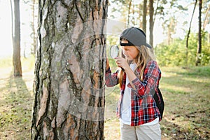 Rear view image of cute little girl exploring the nature with magnifying glass outdoor. Child playing in the forest with