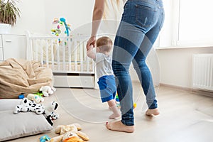 Rear view image of mother holding her baby by hands and teaching making first steps