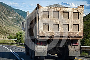 Rear view on a large dump truck rides on a highway in the mountains while transporting goods over long distances. Fast delivery by