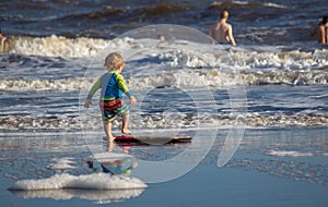 Rear view of a little boy standing on the beach and trying to stand on the wakeskate photo
