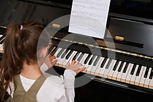 Rear view little child girl performing the rhythm of classical music while playing grand piano, putting fingers on keys