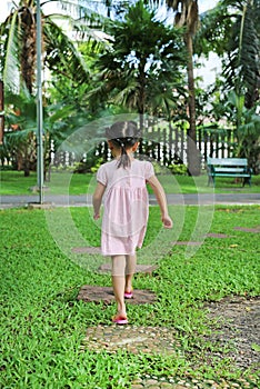 Rear view little child girl walking on stone pathway in the garden at the morning