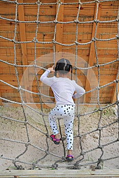 Rear view little kid girl at playground playing on climbing rope net