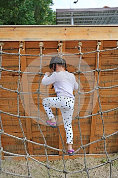Rear view little kid girl at playground playing on climbing rope net