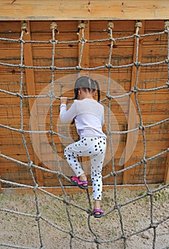 Rear view little kid girl at playground playing on climbing rope net