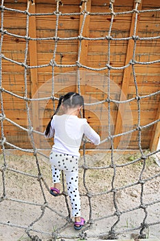 Rear view little kid girl at playground playing on climbing rope net