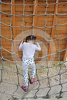 Rear view little kid girl at playground playing on climbing rope net