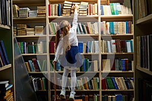 rear view on long haired child girl taking a book from bookshelves in library