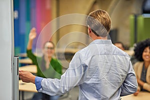 Rear view of a male coach or speaker pointing at giving a presentation to audience during corporate seminar or training