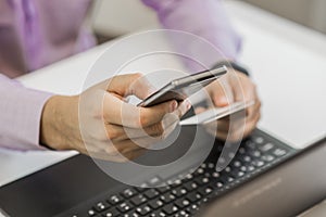 Rear view of male hands holding credit card typing numbers on computer keyboard while sitting at home at the table