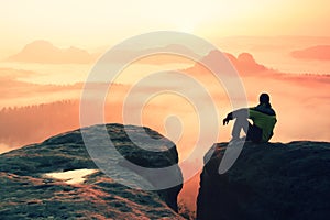 Rear view of male hiker sitting on the rocky peak while enjoying a colorful daybreak above mounrains valley